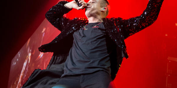 Macklemore sings into microphone on stage in front red spot lights at the BJC in 2013.