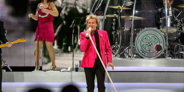Rod Stewart, wearing a bright pink blazer & tie, sings into a white standing microphone during his concert at the BJC in 2013.