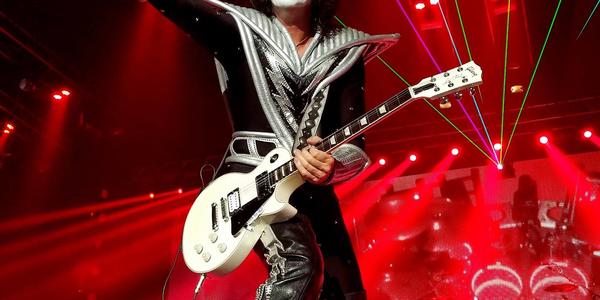 KISS guitarist performs in red stage lighting and smoke, points to the crowd at the BJC in 2016
